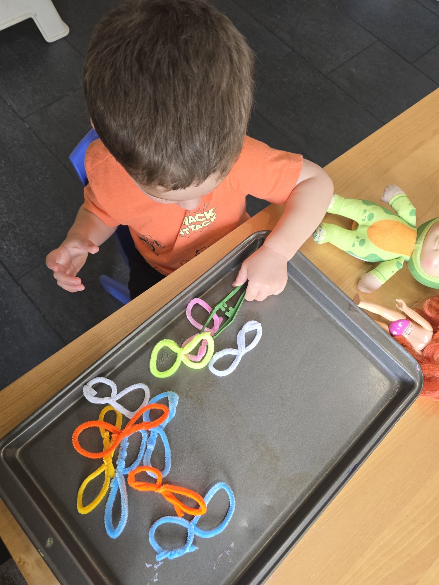 Toddler exploring colourful pipe cleaners shaped into loops on a sensory tray