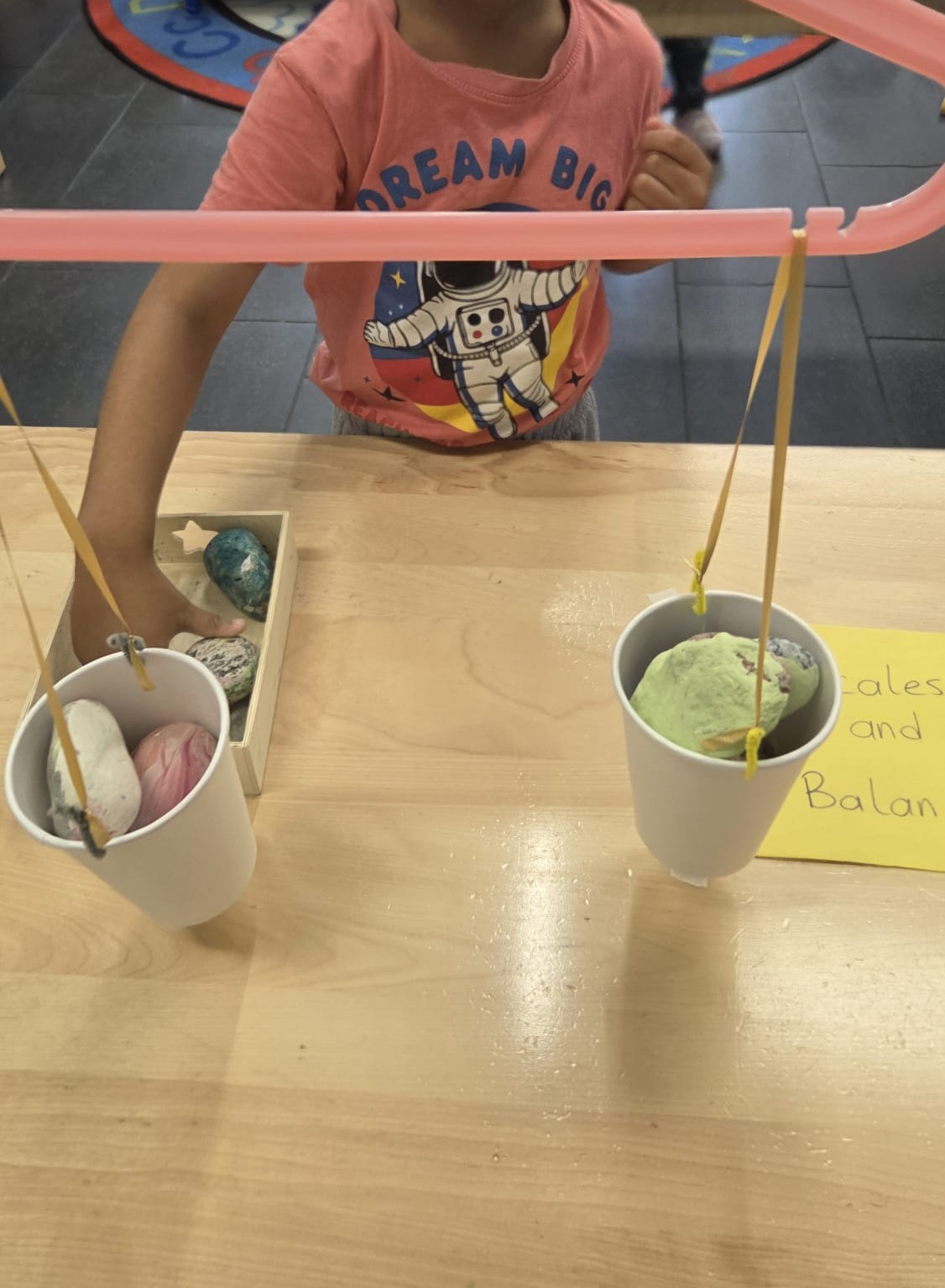 Child comparing painted rocks on a homemade balance scale during a scales and balance activity