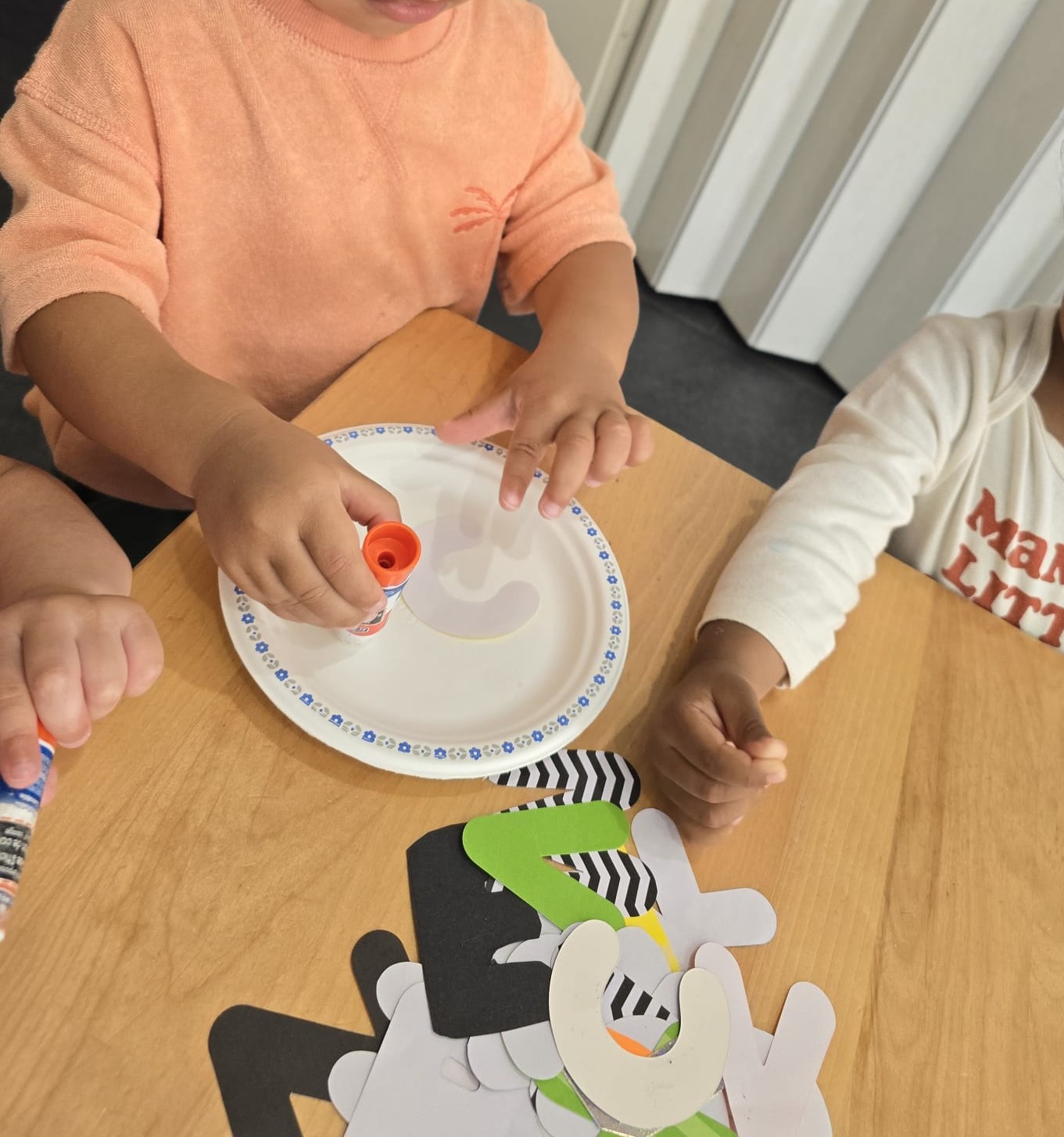 Preschoolers using glue sticks to make a paper collage together at a wooden table