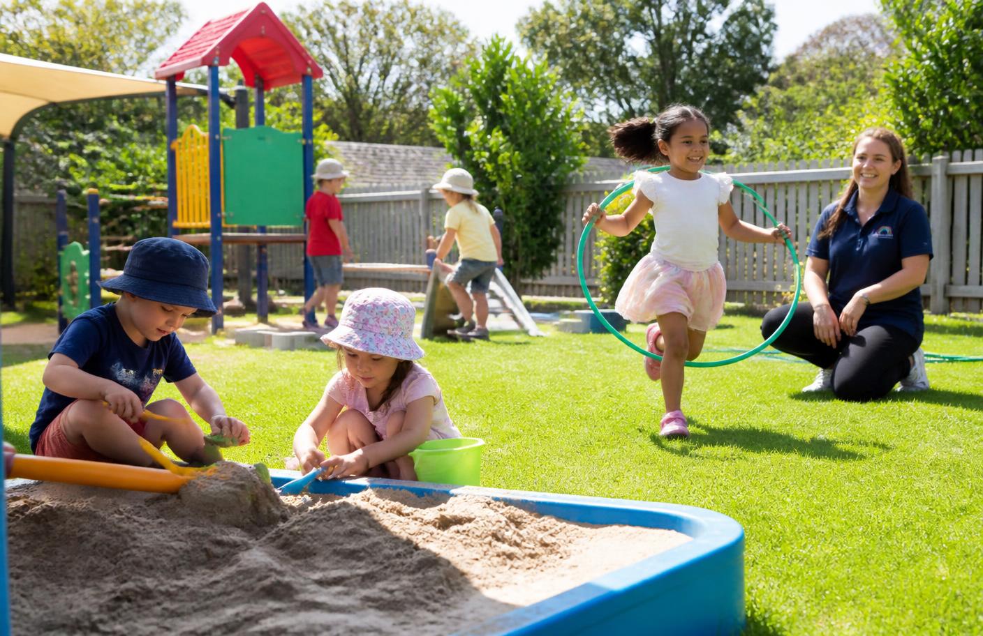Children digging in the sandbox and running with a hoop in a sunny fenced playground